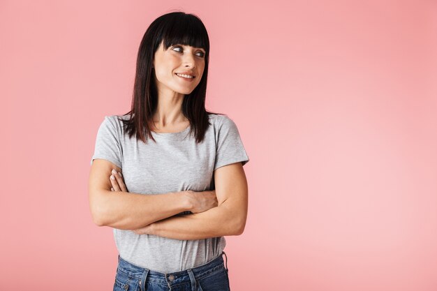 Séduisante jeune femme brune souriante debout isolée sur un mur rose, les bras croisés