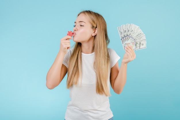 Séduisante jeune fille blonde avec des jetons de poker du casino en ligne et de l'argent isolé sur bleu