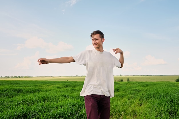 Séduisante jeune homme dans un t-shirt blanc se tenant dans un champ de blé vert jeune, profitant de la nature