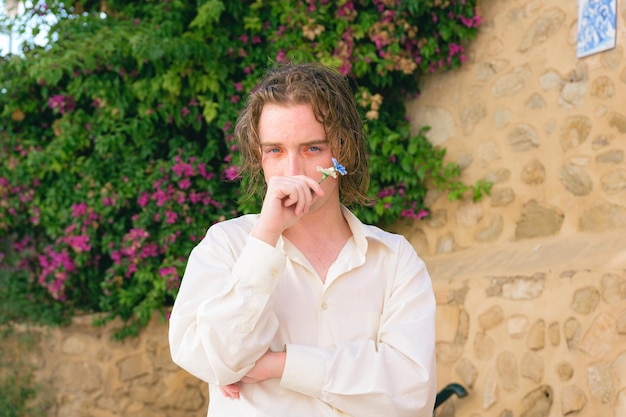 Séduisante jeune homme avec des poses de maquillage avec des fleurs en regardant la caméra