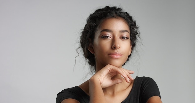 Séduisante jeune mannequin du Moyen-Orient touchant son joli visage avec une peau impeccable et souriante