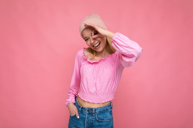 Séduisante souriante heureuse jeune femme blonde debout isolée sur un mur de fond coloré portant