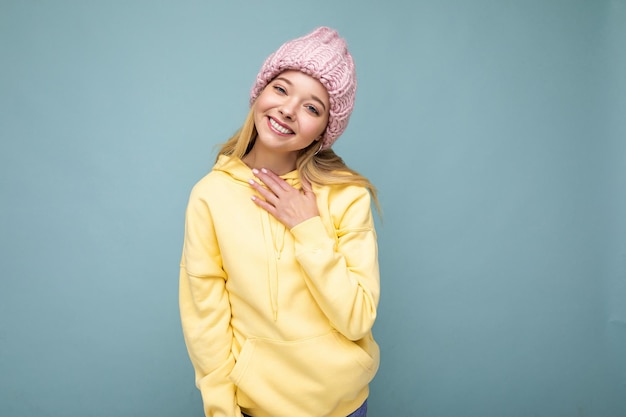 Séduisante souriante heureuse jeune femme blonde debout isolée sur un mur de fond coloré portant