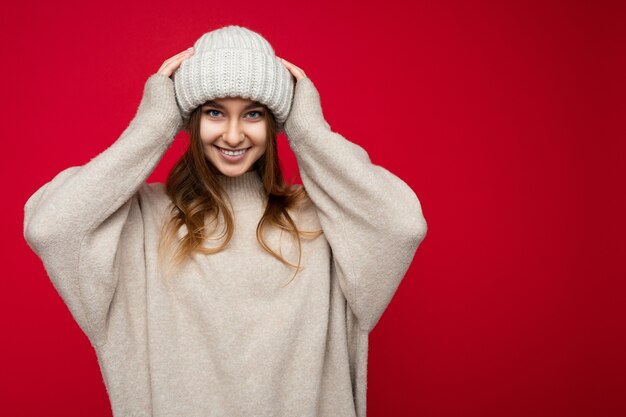 Séduisante souriante heureuse jeune femme blonde foncée debout isolée sur un mur de fond coloré portant une tenue élégante de tous les jours montrant des émotions faciales en regardant la caméra. Espace libre