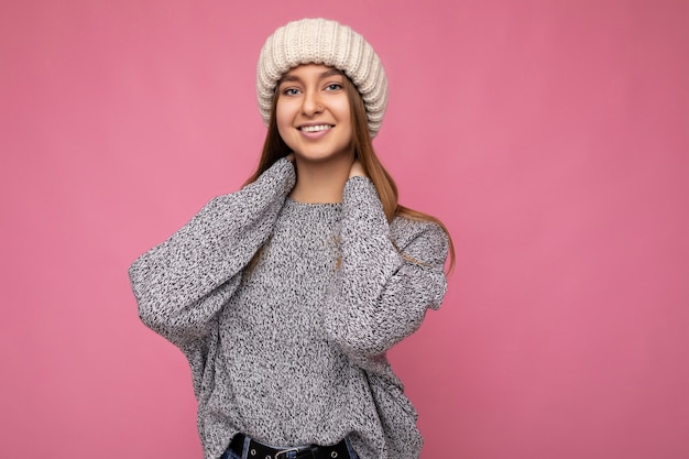 Séduisante souriante heureuse jeune femme blonde foncée debout isolée sur un mur de fond coloré portant une tenue élégante de tous les jours montrant des émotions faciales en regardant la caméra