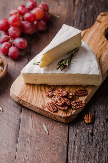 Segment de camembert français sur planche de bois avec raisins et noix de pécan