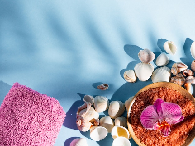 Sel de bain orange dans une soucoupe avec coquillages, serviette et fleur sur fond bleu avec une ombre d'une plante tropicale. Copyspace, flatlay. Spa, détendu, été