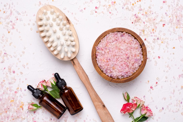 Photo sel de bain à la rose, masseur et bouteilles d'huile naturelle sur blanc