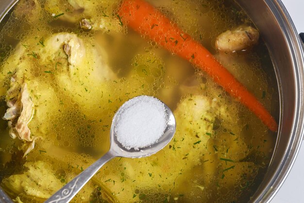 Le sel est ajouté au bouillon de poulet avec une cuillère métallique