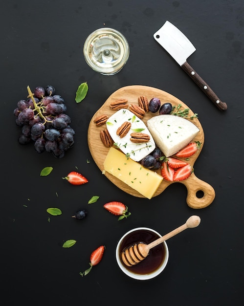 Sélection d'apéritifs au fromage ou ensemble de collations de gémissement Variété de raisins au fromage noix de pécan fraise et miel sur planche de bois ronde sur fond noir