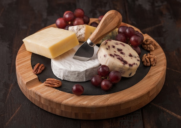 Sélection de divers fromages sur le plateau et raisins sur fond de table en bois. Blue Stilton, Red Leicester et fromage Brie avec un couteau sur une planche à découper ronde.