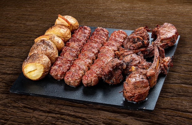 Une sélection de diverses viandes gastronomiques au barbecue sur un tableau noir avec un fond de bois rustique Carré d'agneau kebab de pommes de terre