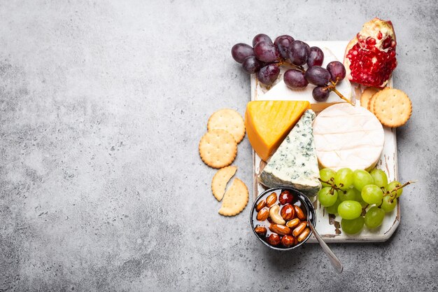 Sélection de fromages et apéritifs, camembert, brie, cheddar, pain, cracker, raisins, noix, miel. Mélange assorti de fromages sur planche de bois rustique avec un espace pour le texte, vue de dessus, gros plan