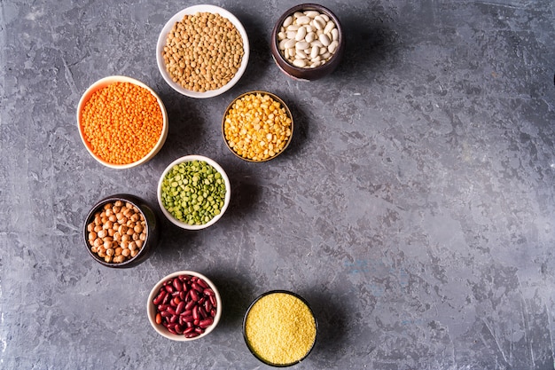 Sélection de légumineuses. haricots, lentilles, pois chiches, pois dans des bols sur fond de béton gris.