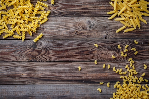 Sélection de pâtes séchées mixtes sur fond de bois. Vue de dessus à plat avec espace de copie pour texte, logo ou autre.