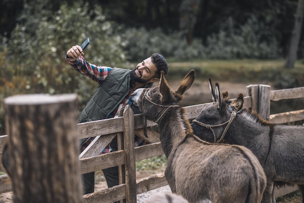 Selfie. Agriculteur gai faisant le selfie avec des ânes