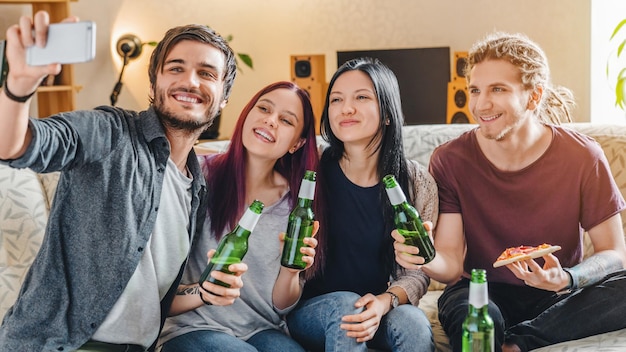 Selfie d'amis multiethniques heureux faisant la fête à la maison avec de la pizza et de la bière