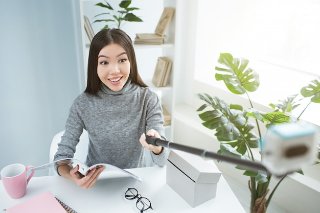 Selfie d'une femme assise à la table et tenant un journal dans ses mains