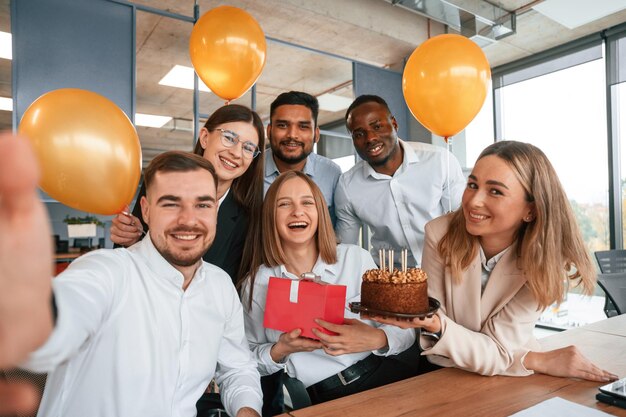 Selfie d'une femme heureuse avec un cadeau Employé ayant un anniversaire dans le groupe de travailleurs du bureau