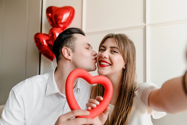 Selfie d'homme et femme amoureux de coeur et de ballons rouges à la maison