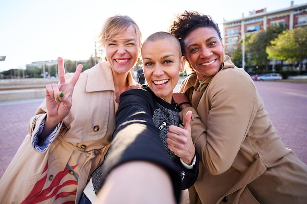 Photo selfie mobile de trois femmes multiraciales d'âge moyen qui regardent une caméra souriante en groupe en plein air