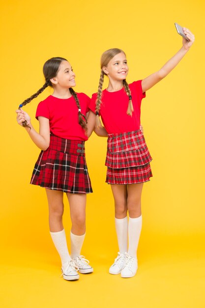 Selfie pose de petites filles faisant selfie au téléphone s'amusant fraternité et amitié heureuse journée de la connaissance bonheur de l'enfance concept d'éducation retour à l'école réseau social filles en uniforme