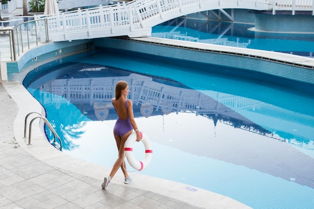 Selfieportrait en gros plan d'une jolie fille aux cheveux longs debout près de la piscine Elle sourit à la caméra et montre un look cool Chapeau de paille sur la tête En vacances de villégiature