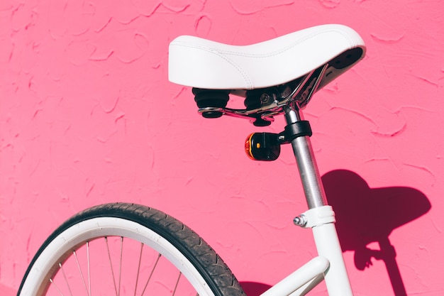 Selle blanche d'un vélo de ville féminin sur fond de mur rose