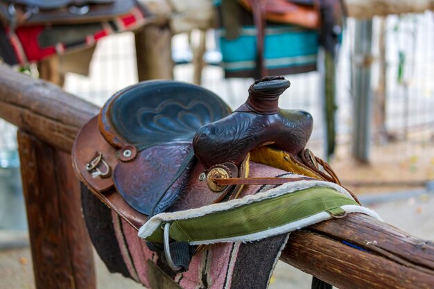 Selle sur clôture contre le mur en bois. Selle de sport en cuir, harnais pour chevaux à la lumière du jour. Selles de cheval western sur un rack, prêtes pour l'entraînement de dressage. Fond de sport équestre, vintage.