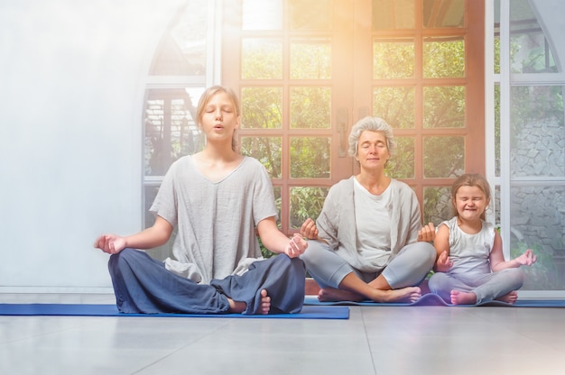 Senior avec adolescent et petits-enfants faisant du yoga à la maison