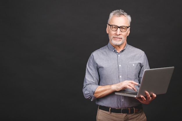 Senior âgé barbu vieillard à lunettes tenant un ordinateur portable à la recherche et souriant.