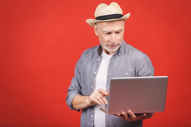 Senior âgé barbu vieillard en tenue décontractée et chapeau tenant un ordinateur portable isolé.