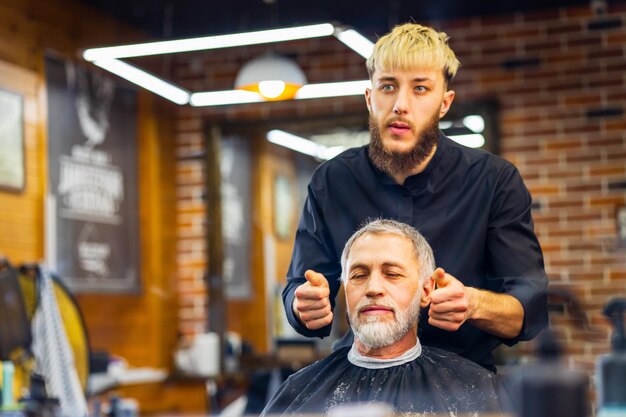 Senior bel homme visitant un coiffeur dans un salon de coiffure moderne