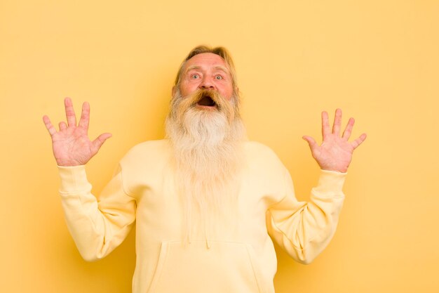 Senior cool barbu se sentant stupéfait et effrayé craignant quelque chose d'effrayant avec les mains ouvertes devant disant rester à l'écart