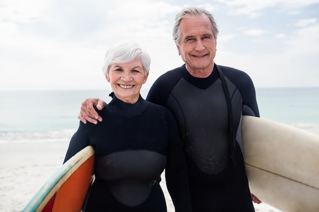 Senior couple en combinaison de surf tenant la planche de surf sur la plage