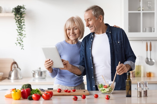 Senior couple reading food blog on digital tablet cooking