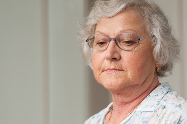 Senior femme âgée regardant vers le bas avec tristesse, gros plan intérieur tourné