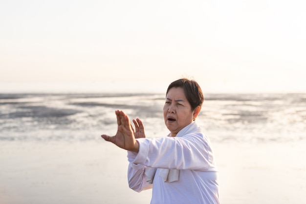 Senior femme asiatique pratiquant l'exercice de Tai Chi pendant le coucher du soleil à la plage