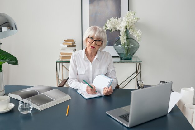 Senior femme cheveux gris en blouse blanche la lecture de documents au bureau