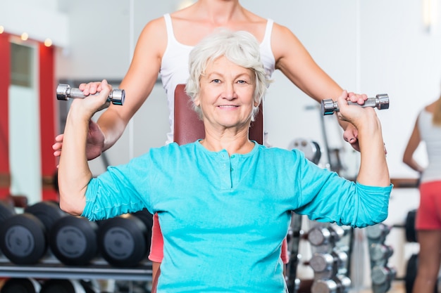 Senior femme avec entraîneur en gym soulevant des haltères