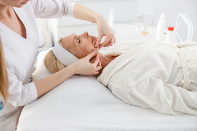 Senior femme est allongée sur le dos, se fait masser le visage. Soin de beauté de massage du visage.