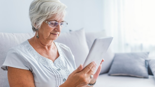 Senior femme avec des lunettes de navigation sur tablette numérique