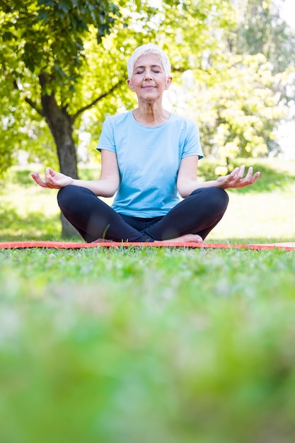 Senior femme en posture de lotus assis sur l&#39;herbe verte