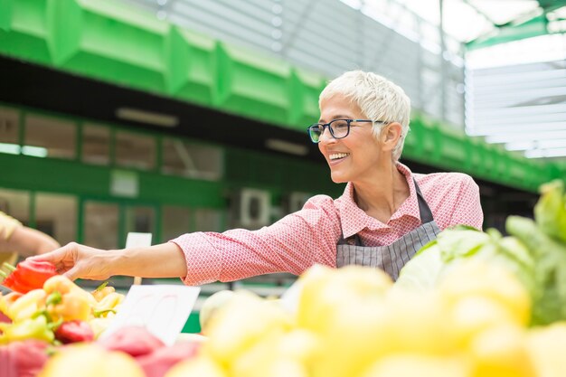 Senior femme vend des légumes sur le marché