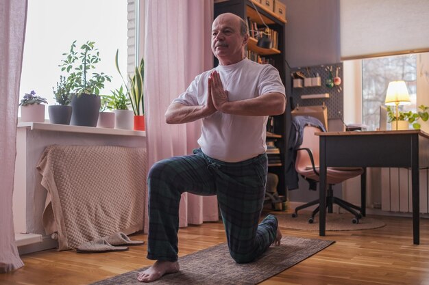 Senior hispanic man standing in warrior deux pose de yoga pratiquant seul dans le salon