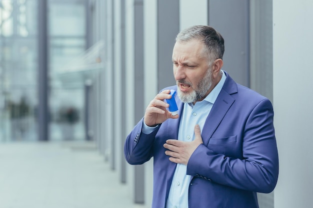 Senior homme d'affaires aux cheveux gris malade a une crise d'asthme difficile à respirer l'homme à l'extérieur du bureau