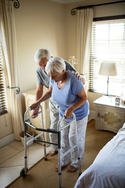 Senior homme aidant la femme à marcher avec un déambulateur à la maison