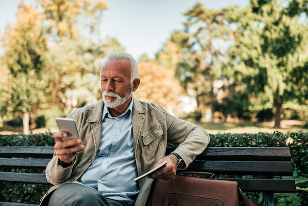 Senior homme assis sur le banc et à l&#39;aide de smartphone.