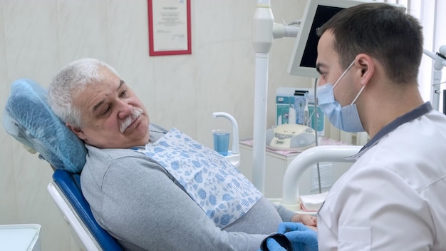 Senior homme assis sur une chaise de dentiste et écouter le médecin Dentiste et patient dans un cabinet dentaire