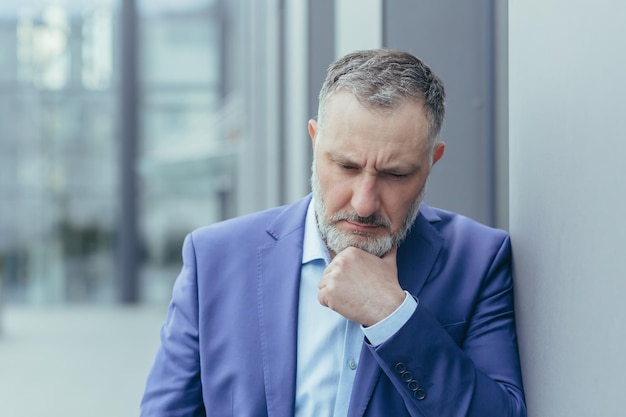 Senior homme aux cheveux gris à l'extérieur de l'immeuble de bureaux debout et pensant homme d'affaires confus et triste